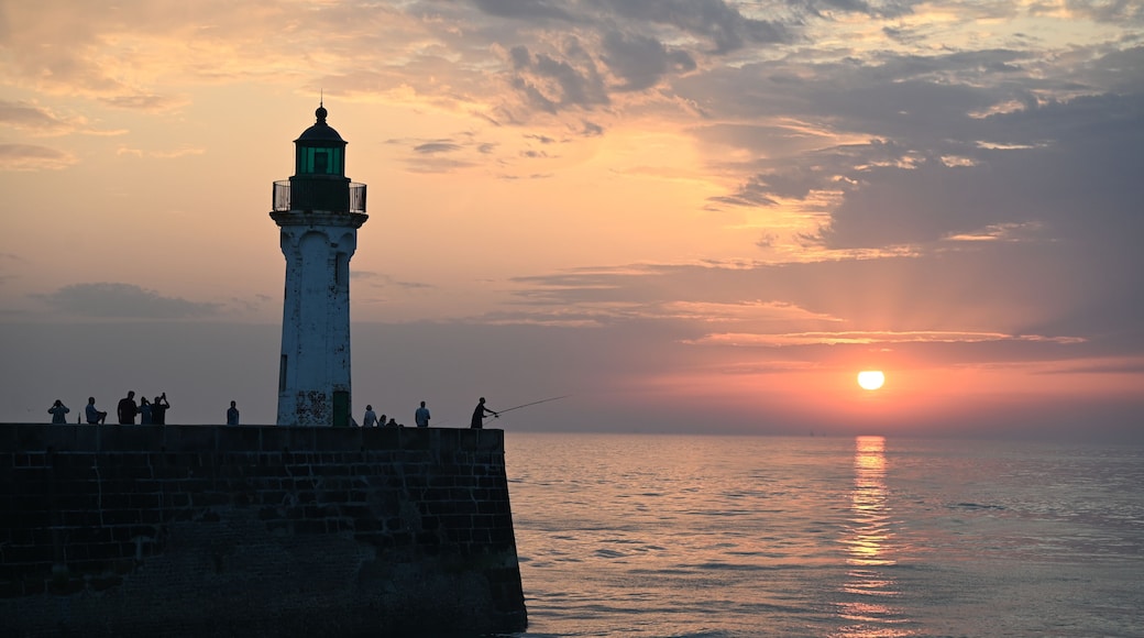 Un faro al atardecer con gente pescando en el muelle.