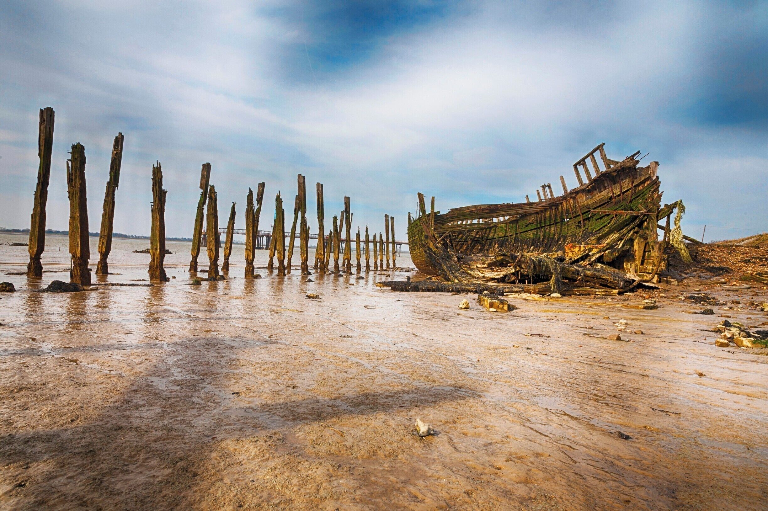A weathered boat on a sandy beach with wooden posts in the background.
