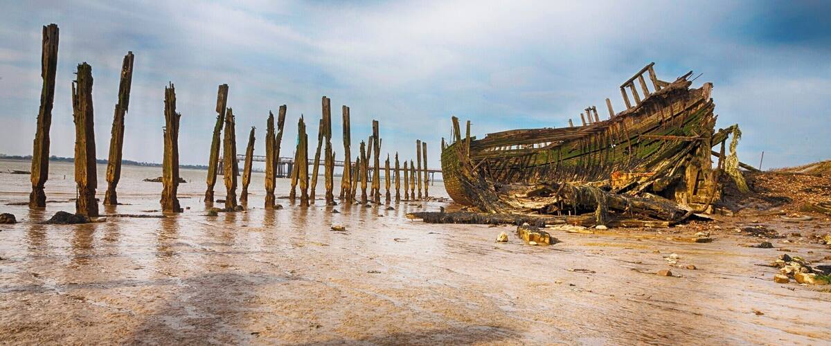 A weathered boat on a sandy beach with wooden posts in the background.