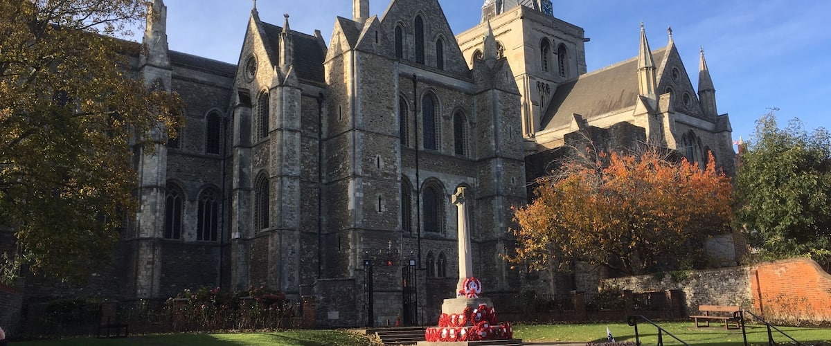 A historic building with a tall spire and a memorial statue in front.