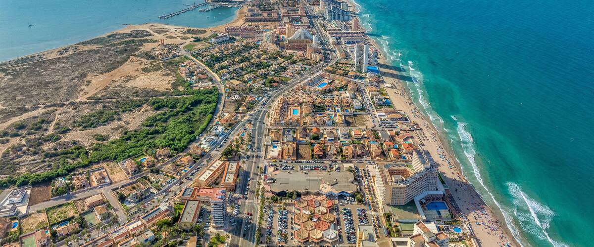 An aerial view of a coastal city with a beach, marina, and urban landscape.