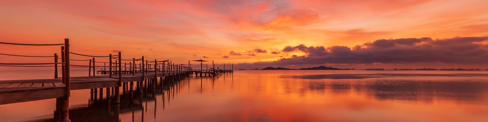 A wooden pier extending into calm waters, reflecting a sunset sky with orange and pink hues.