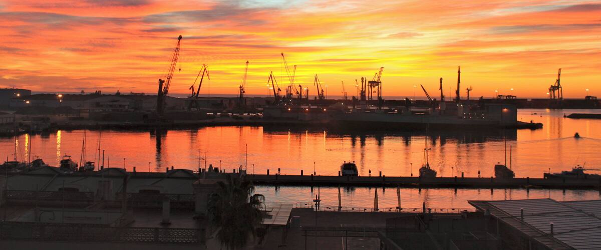 A sunset over a harbor with cranes and ships.
