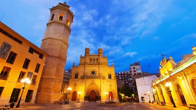 Una catedral histórica con un campanario, rodeada de calles e edificios bien iluminados.