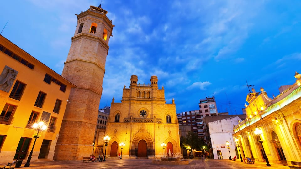A historic cathedral with a bell tower, surrounded by well-lit streets and buildings.