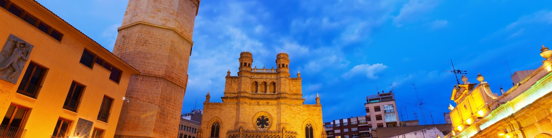 Una catedral histórica con un campanario, rodeada de calles e edificios bien iluminados.