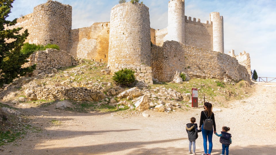 An ancient stone castle with multiple towers and a dirt path leading to it.