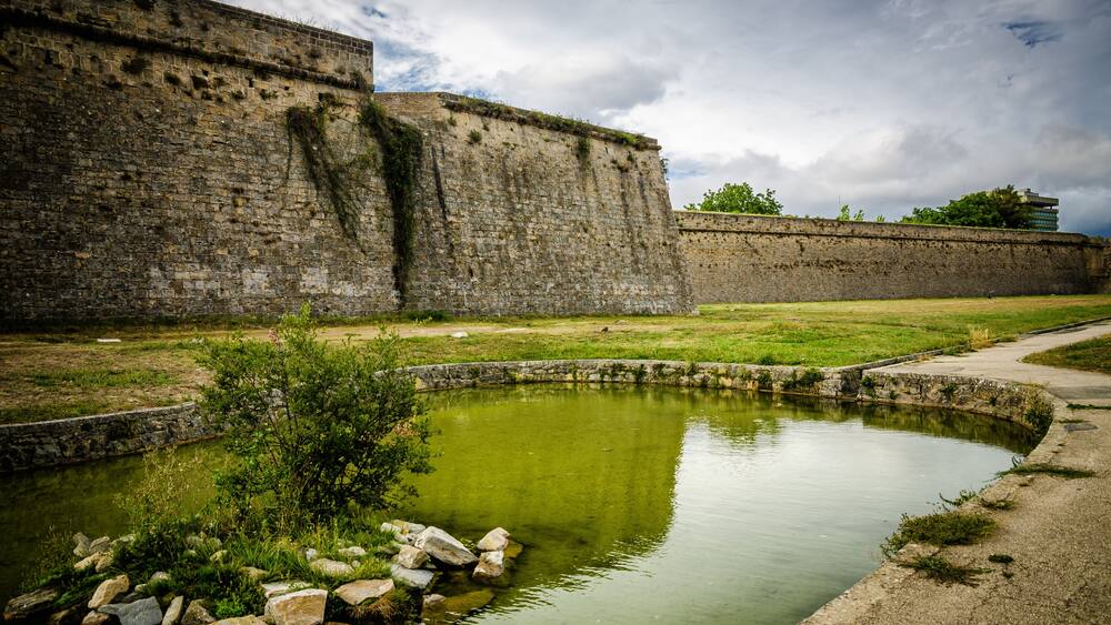 Eine historische Steinmauer, ein kleiner Teich und eine Rasenfläche.