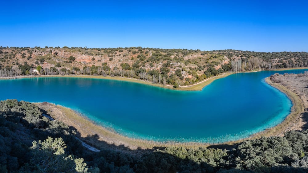 Un lac turquoise, entouré de collines boisées.