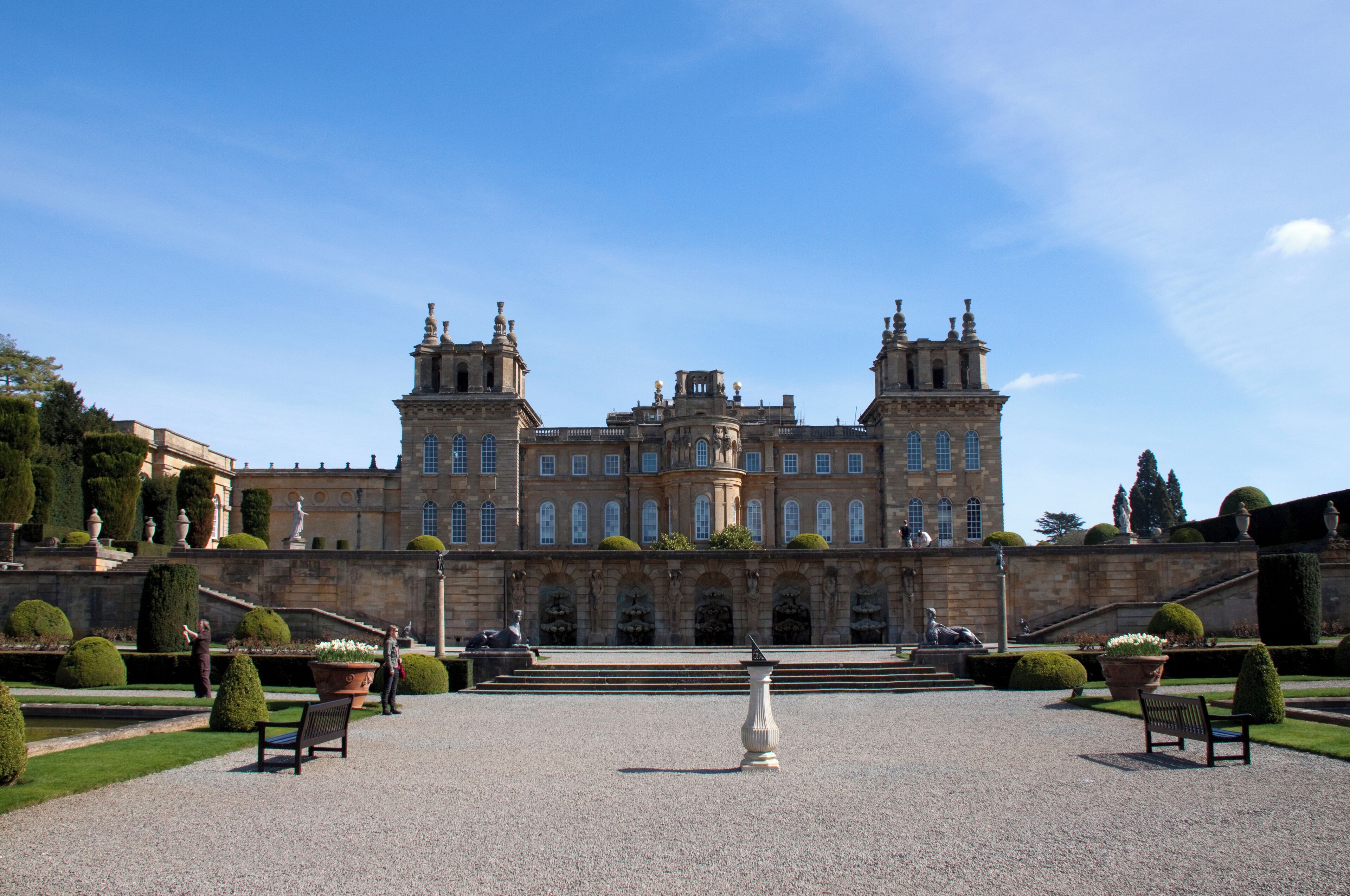 A grand historic building with symmetrical architecture, a central courtyard, and well-manicured gardens.