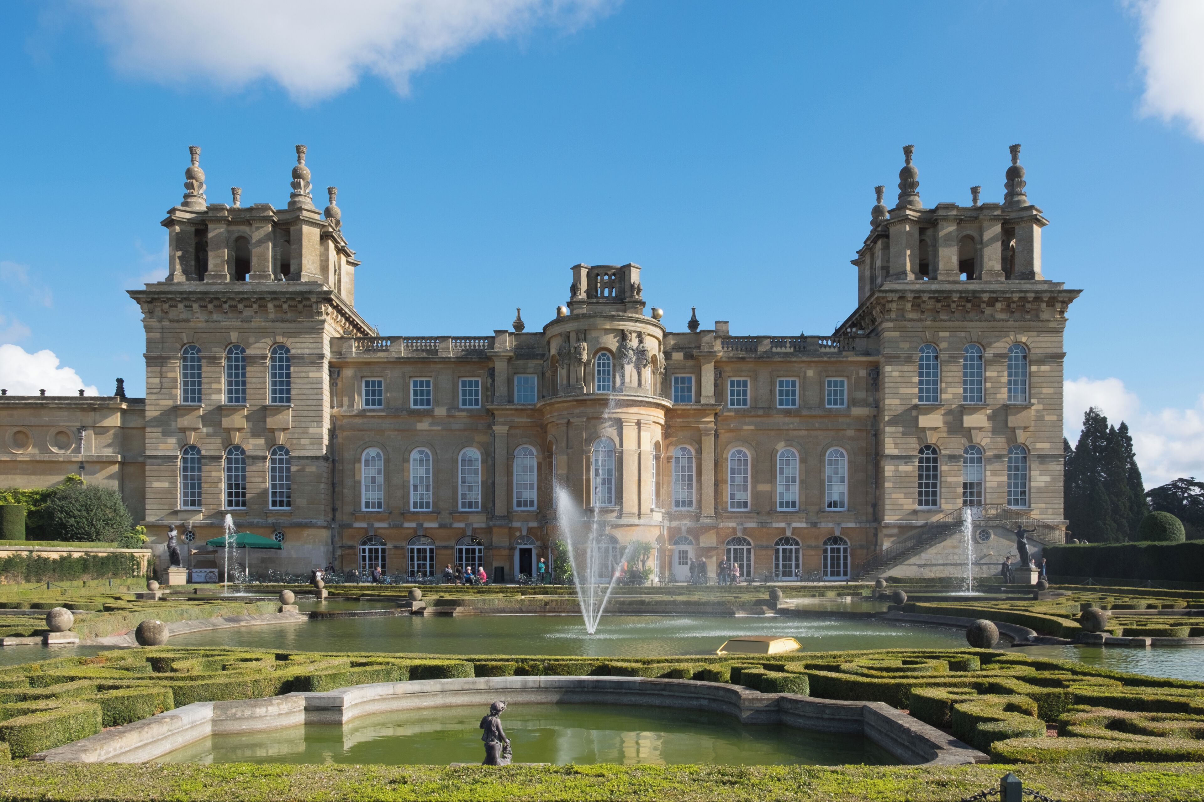 A grand historic building with symmetrical architecture, a central fountain, and manicured gardens.