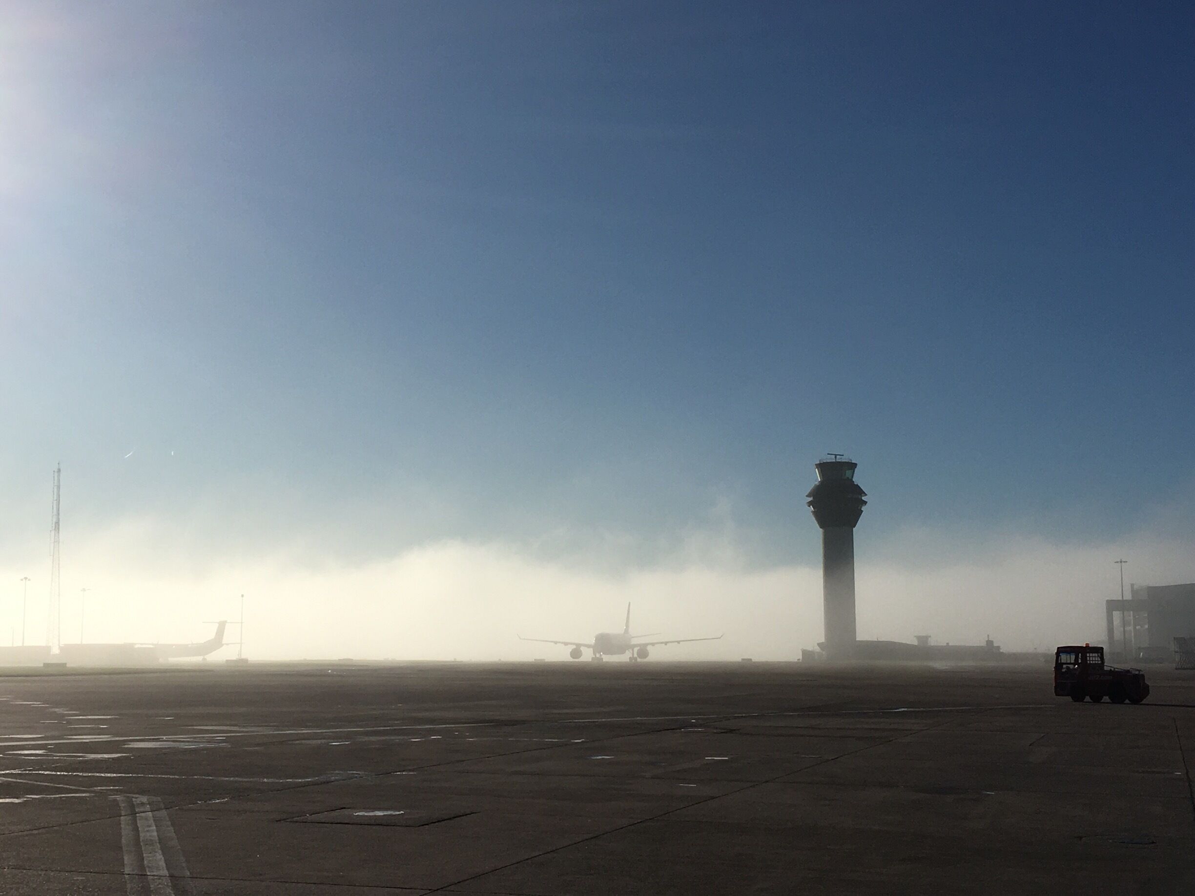 An airport runway with an airplane, a control tower, and a foggy atmosphere.