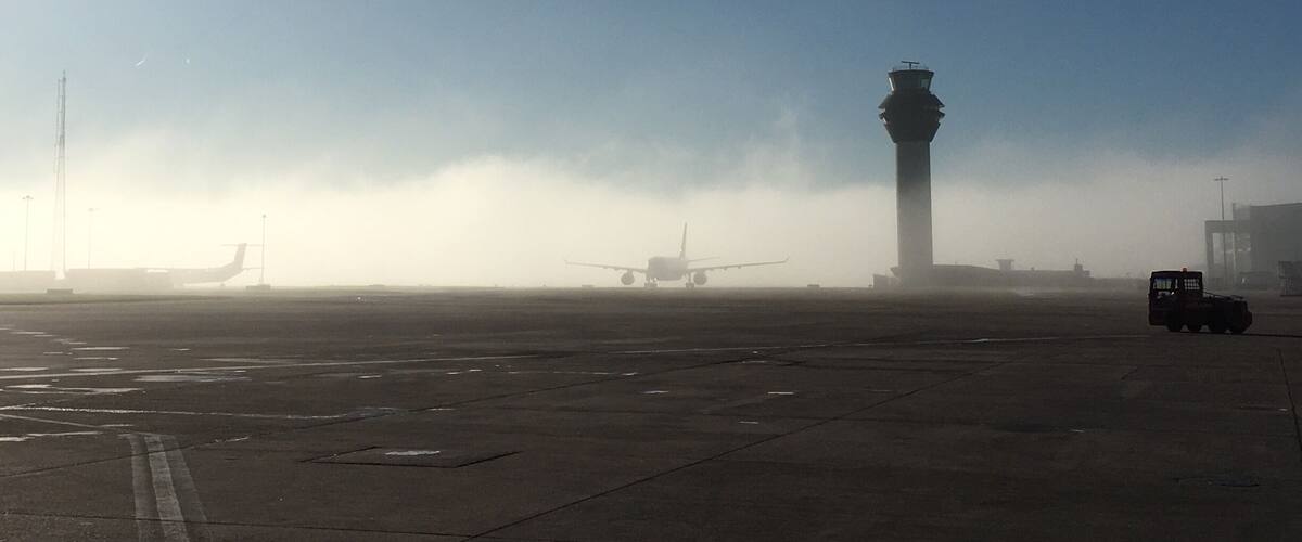 An airport runway with an airplane, a control tower, and a foggy atmosphere.