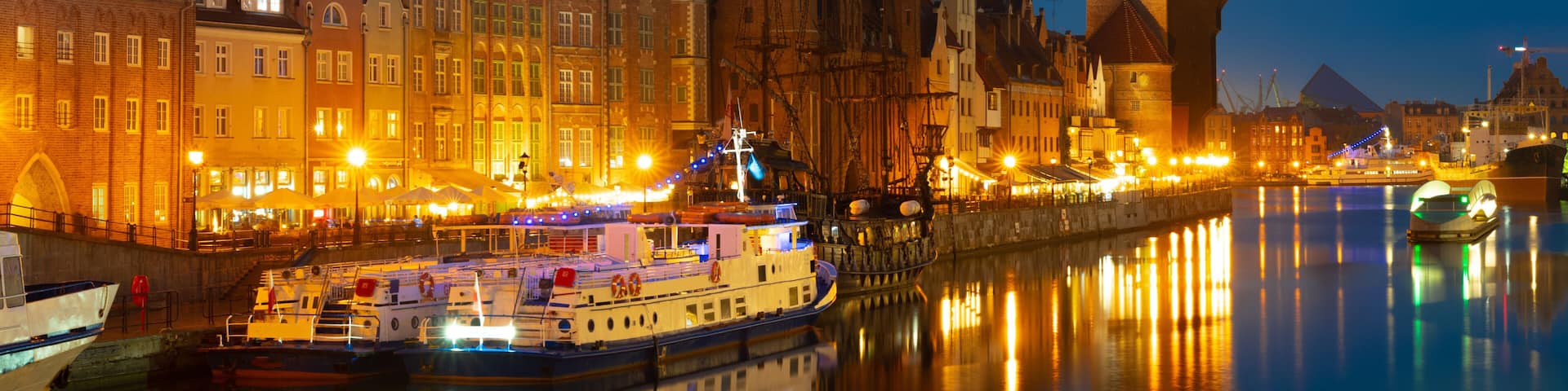A nighttime cityscape with illuminated buildings, a river, and boats.