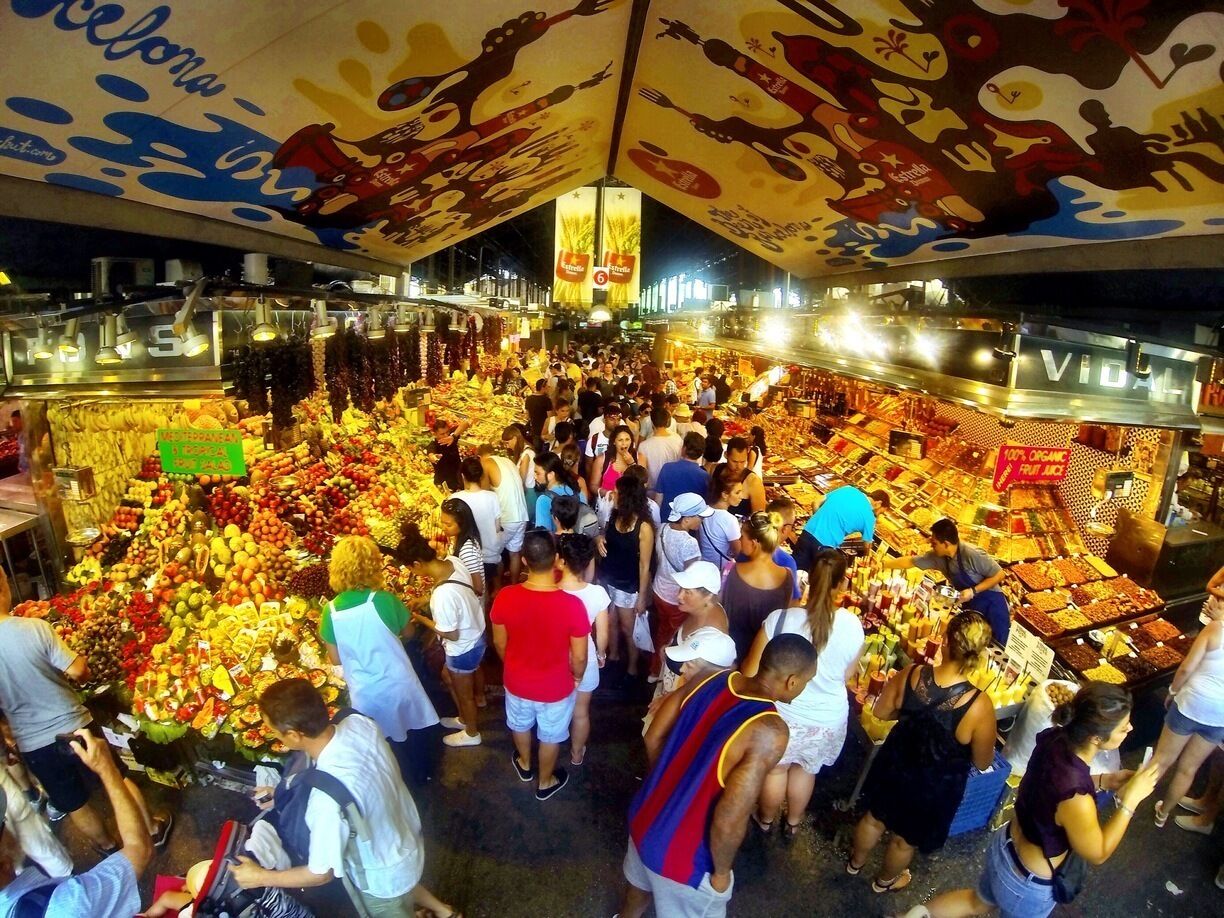Een drukke overdekte markt met verschillende kraampjes waar fruit en groenten worden verkocht.