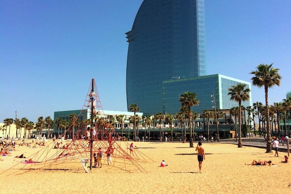 Ein Strand mit Palmen und einem großen, modernen Gebäude mit gewölbter Dachlinie.