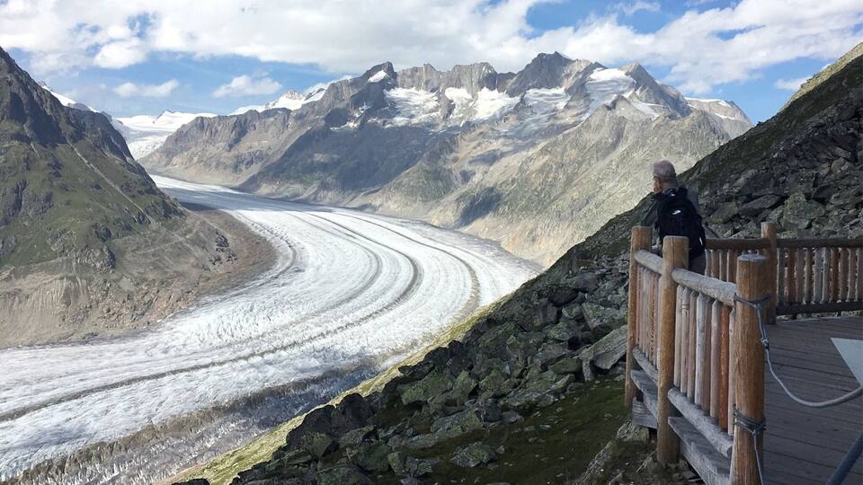 A glacier with a wooden viewing platform and a person observing it.