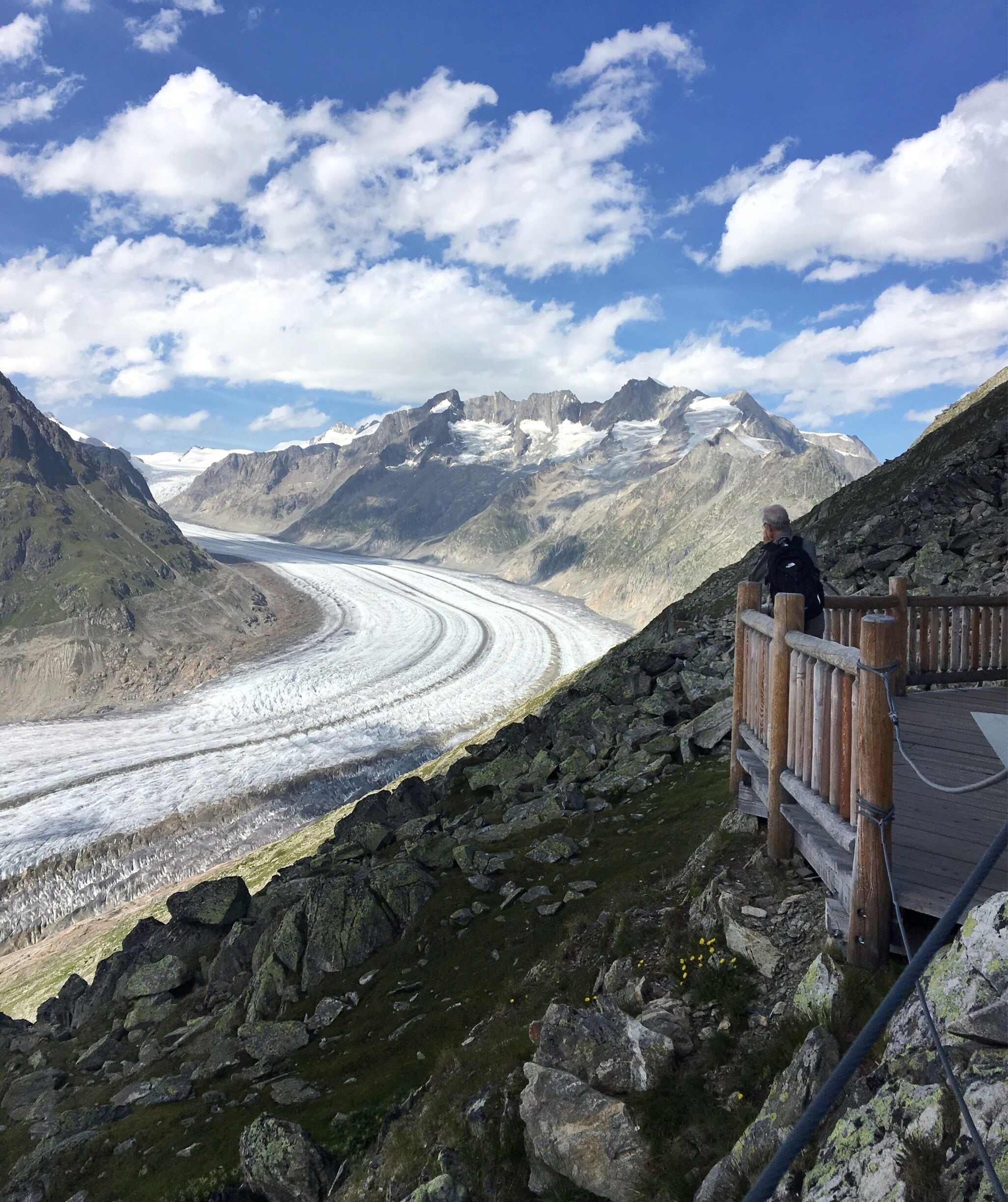 A glacier with a wooden viewing platform and a person observing it.