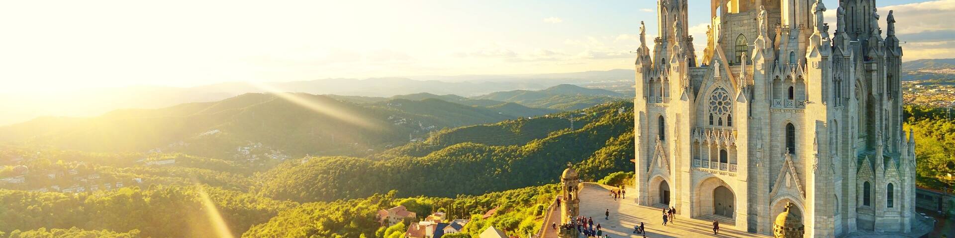 A cathedral with multiple spires, surrounded by lush green hills and a clear sky.