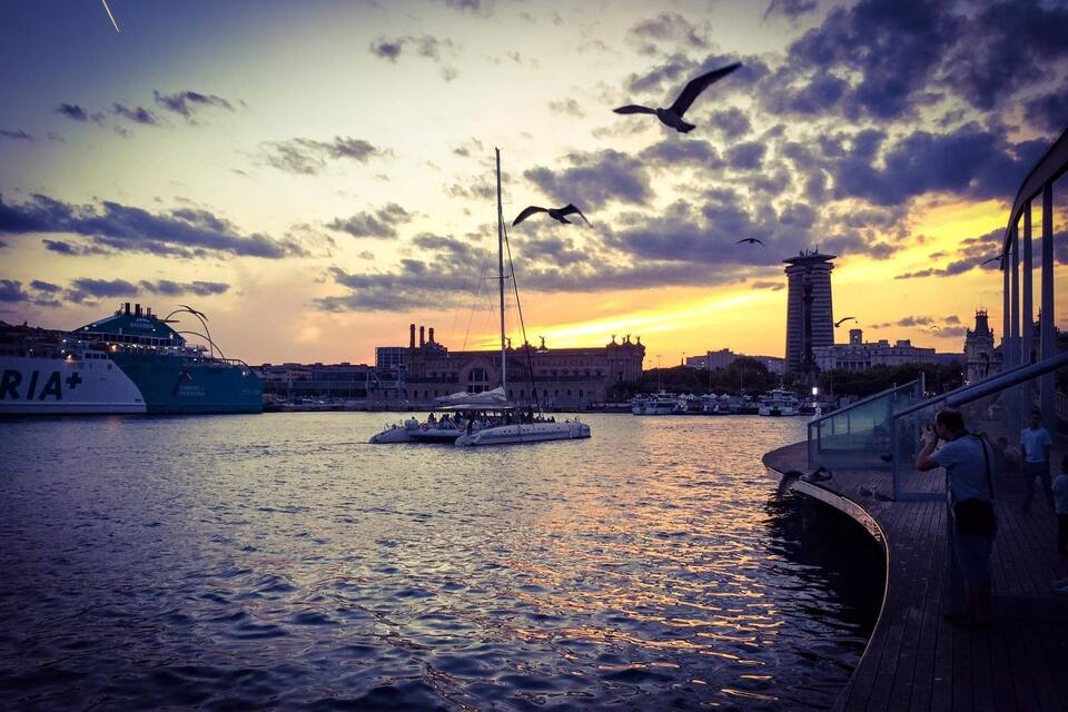 A sunset over a harbor with boats, a tall tower, and a bridge.