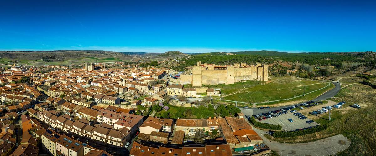 An aerial view of a historic town with a prominent castle, surrounded by a mix of traditional and modern buildings.