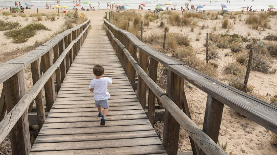 A wooden boardwalk leading to a sandy beach with people and umbrellas.