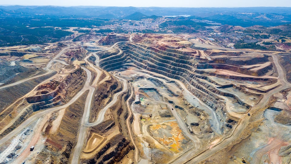 An aerial view of a large open-pit mine with winding roads and terraced excavation areas.