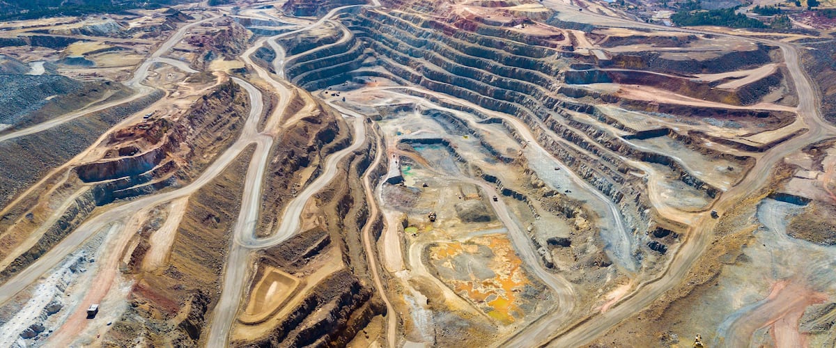 An aerial view of a large open-pit mine with winding roads and terraced excavation areas.