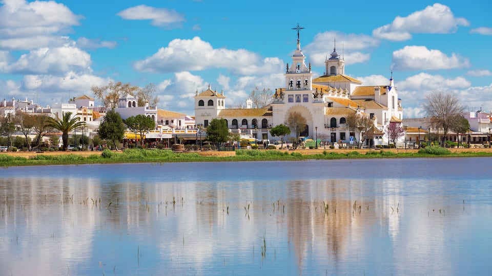 A historic church with multiple domes and a bell tower, reflecting in a calm body of water.