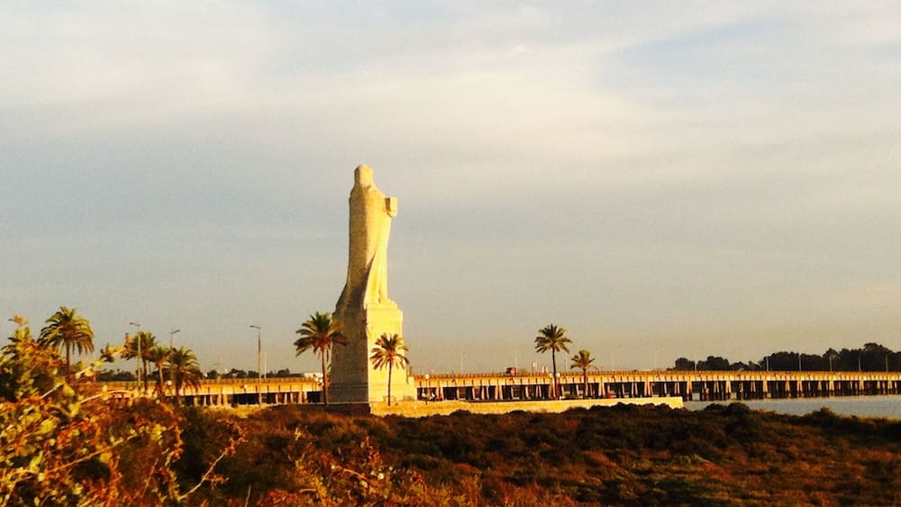 A tall white statue on a hill with a pier extending into the water.