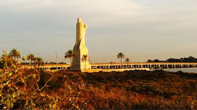 Uma estátua branca e imponente numa colina, com um cais que se estende para a água.