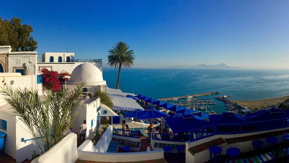 A coastal resort with white buildings, blue umbrellas, and a view of the sea.