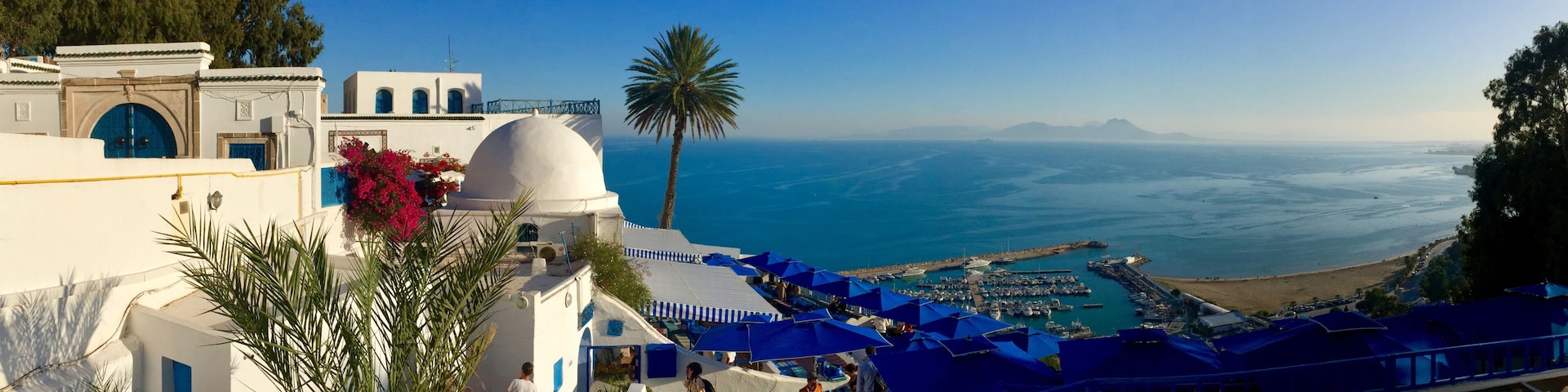 Une station balnéaire avec des bâtiments blancs, des parasols bleus et une vue sur la mer.