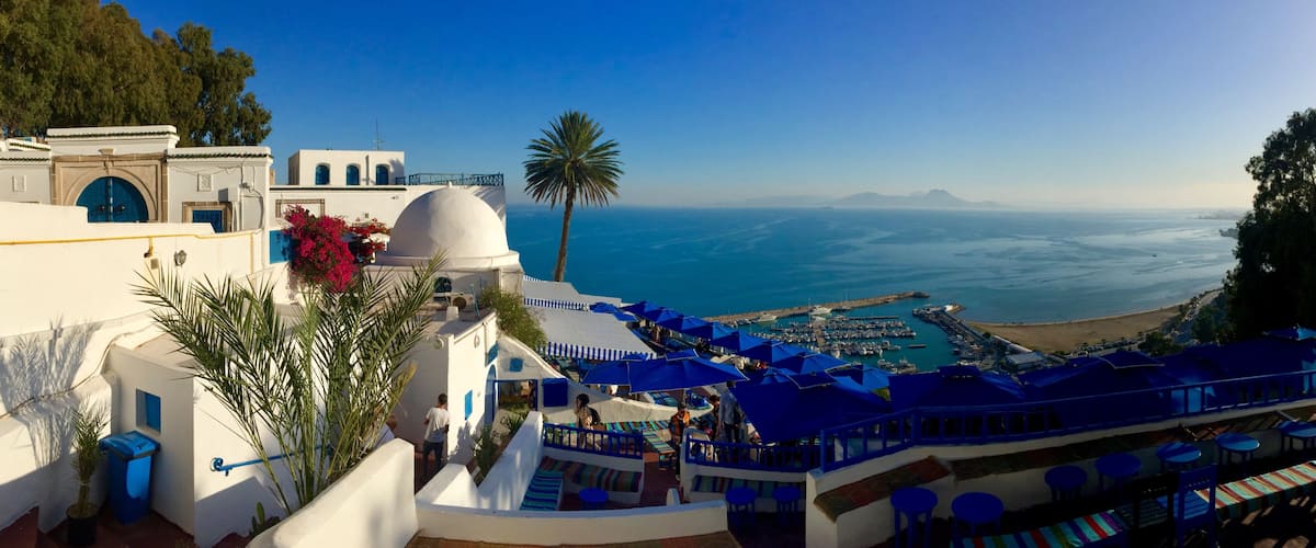 A coastal resort with white buildings, blue umbrellas, and a view of the sea.