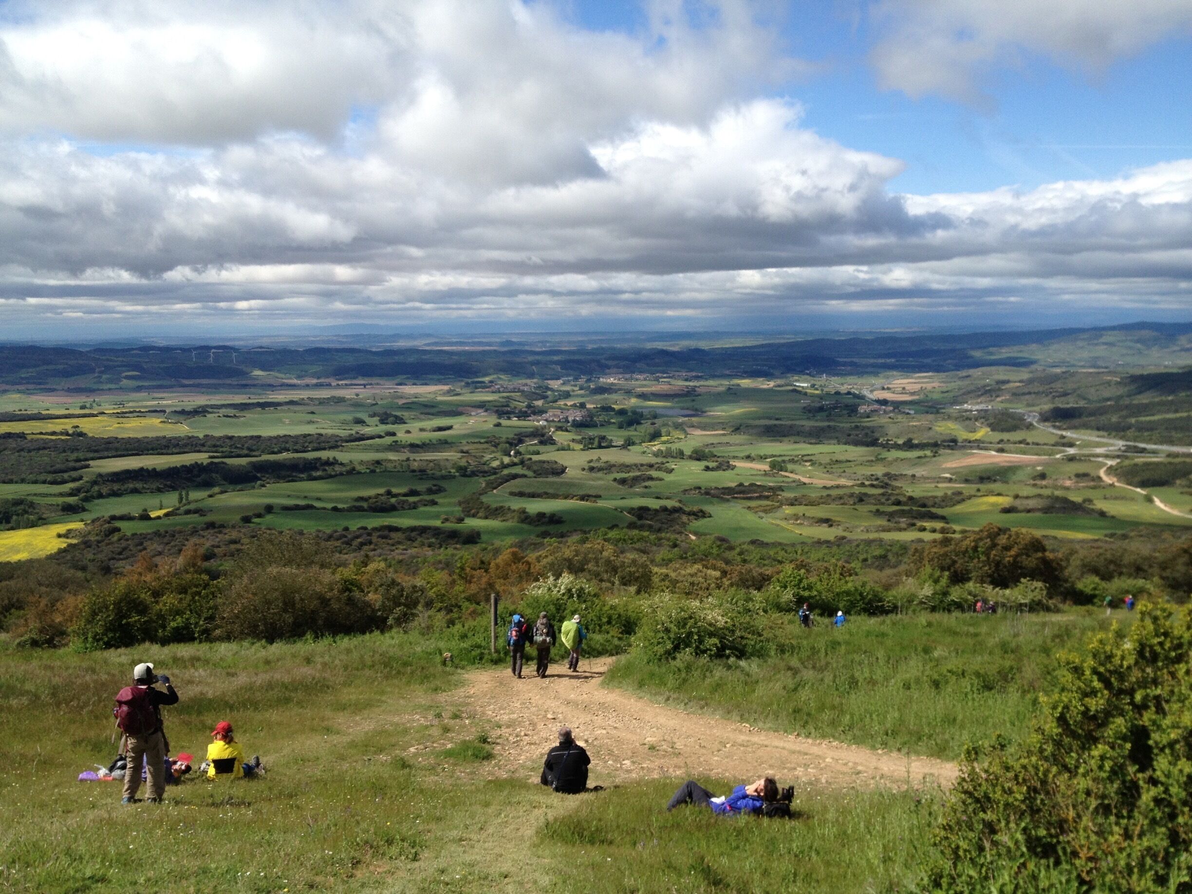 A hilly landscape with a dirt path, people hiking, and a distant view of a valley.