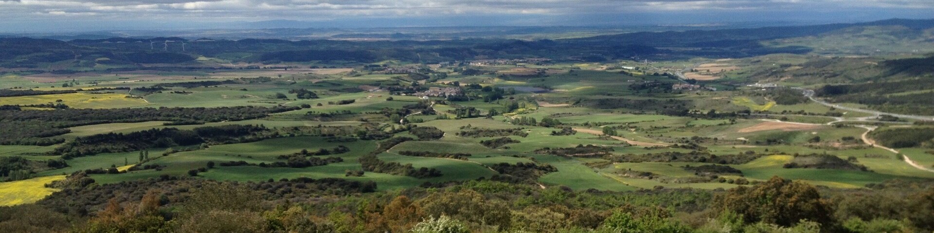 A hilly landscape with a dirt path, people hiking, and a distant view of a valley.