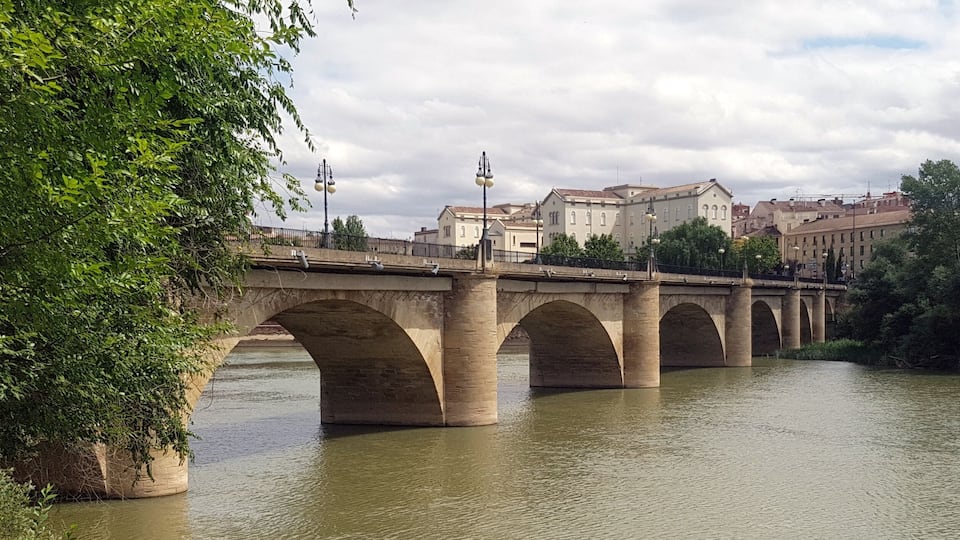 A stone bridge over a river with buildings in the background.