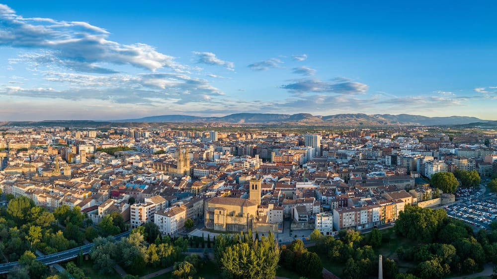A panoramic view of a city with a river, bridges, and mountains in the background.