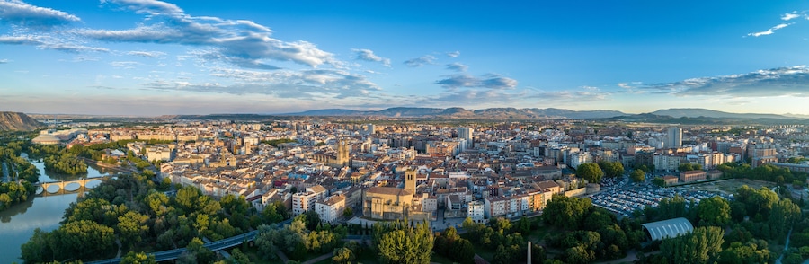 Vista panorámica de una ciudad con un río, puentes y montañas al fondo.