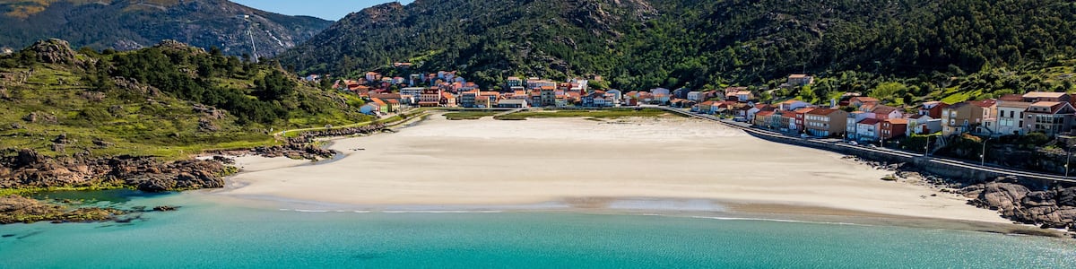 Eine Küstenstadt mit einem Sandstrand, klarem türkisblauem Wasser und Bergen im Hintergrund.