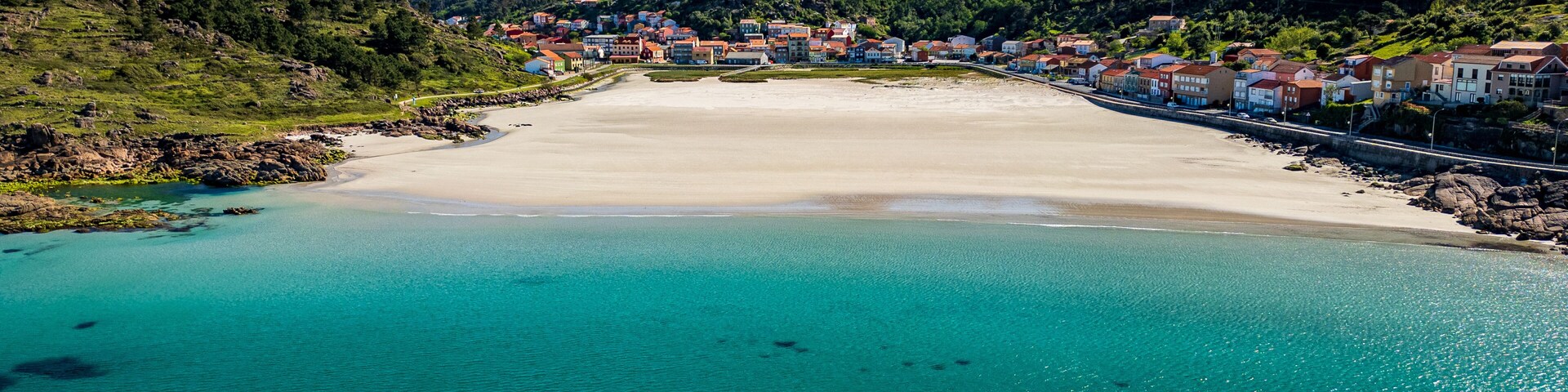 Un pueblo costero con una playa arenosa, aguas turquesas cristalinas y montañas al fondo.