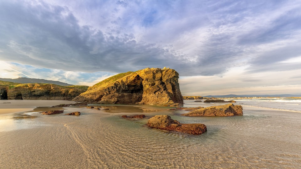 A rocky coastline with a prominent rock formation and calm waves.