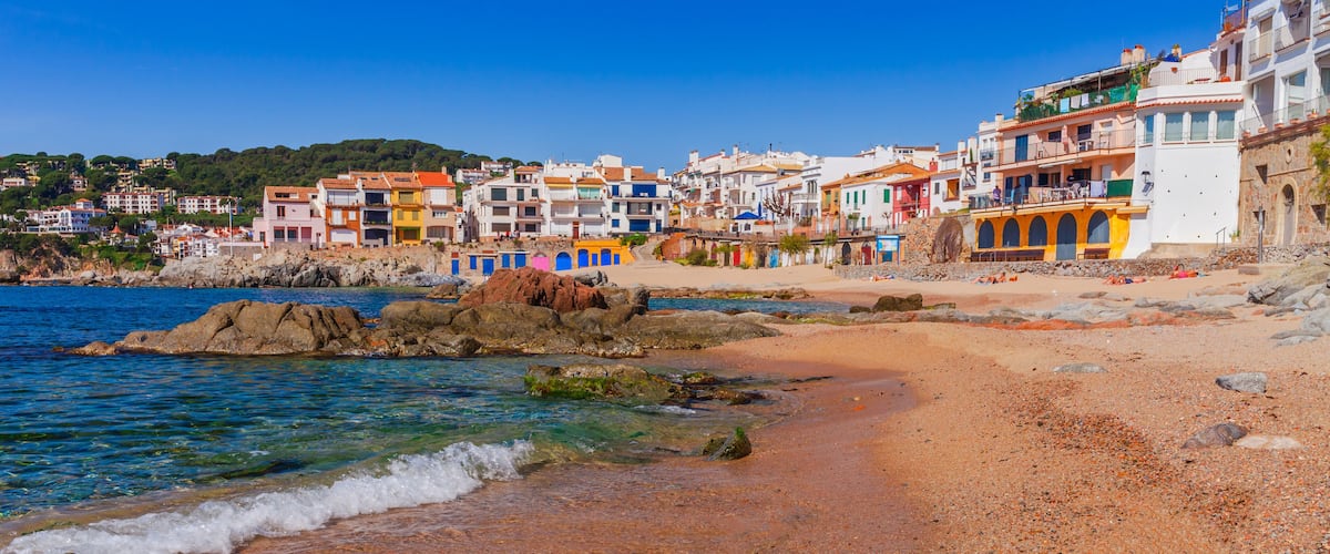 A coastal town with colorful buildings, a sandy beach, and rocky outcrops.