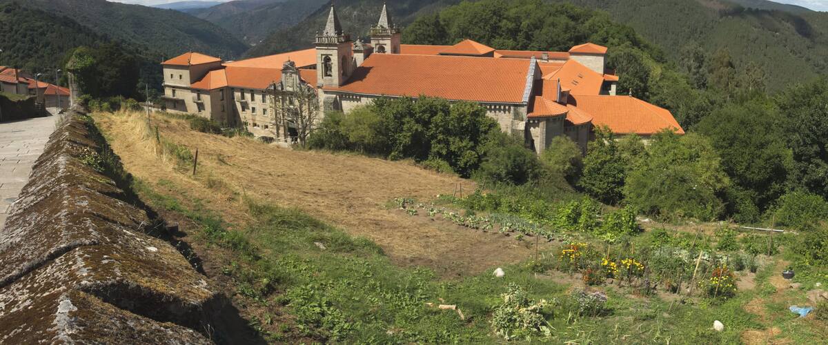 A historic building with red-tiled roofs, surrounded by lush greenery and hills.