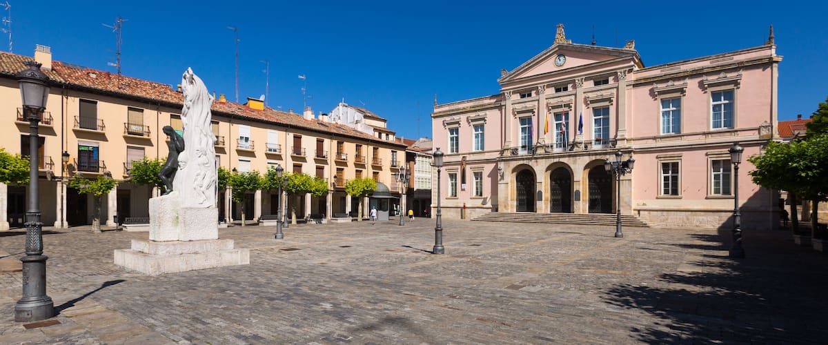 A historic square with a central statue, buildings with classic architecture, and a clear blue sky.