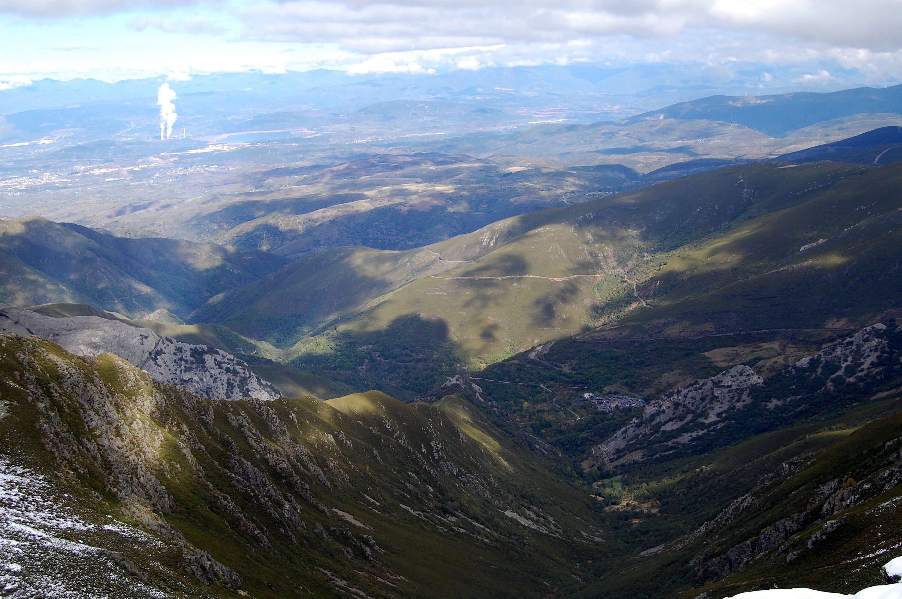 A mountainous landscape with valleys and distant smoke plumes.