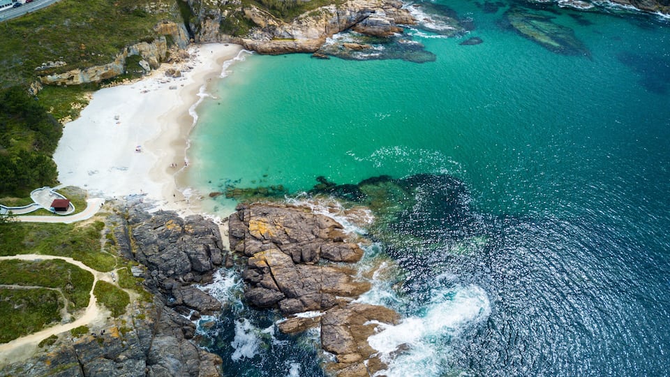 A coastal landscape with a sandy beach, rocky cliffs, and clear turquoise waters.