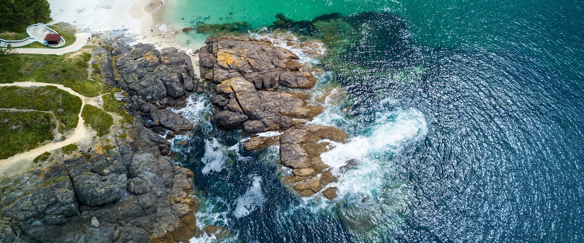 A coastal landscape with a sandy beach, rocky cliffs, and clear turquoise waters.