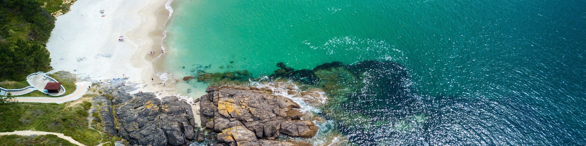 A coastal landscape with a sandy beach, rocky cliffs, and clear turquoise waters.