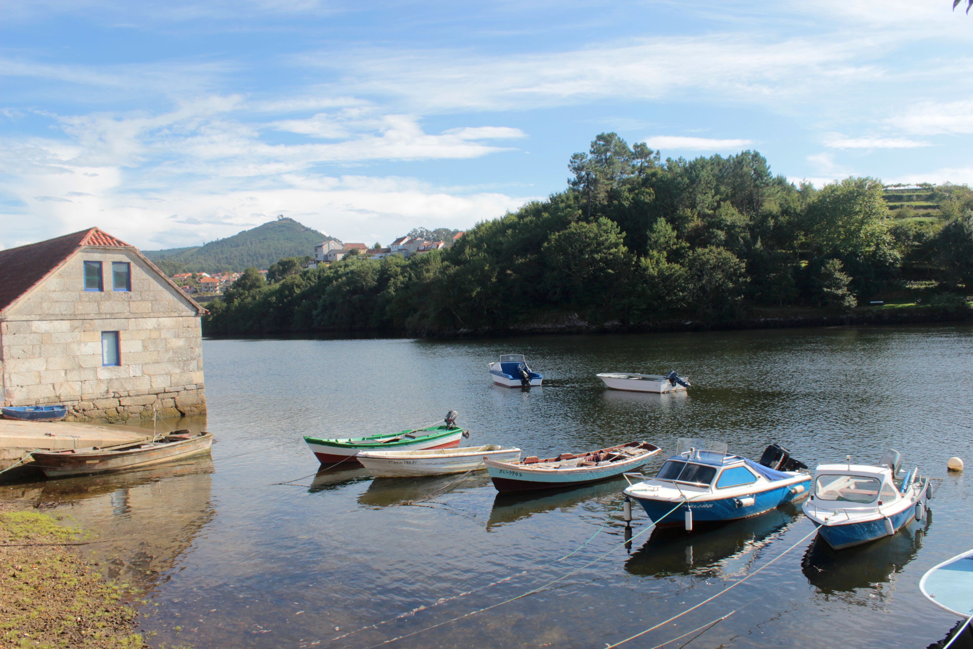 A stone building by a calm river with several small boats docked.